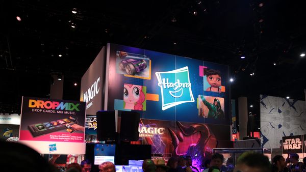 A massive lit-up sign with the tilted blue "Hasbro" logo and cartoon images looms over a dark room.