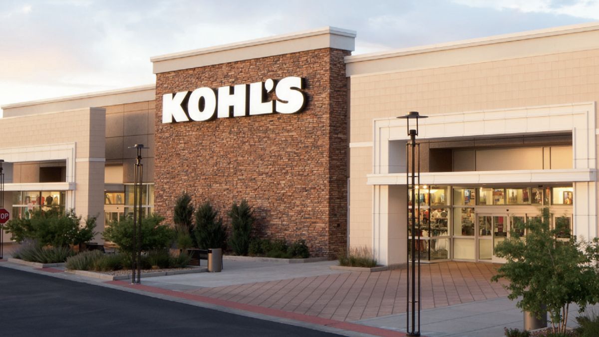 A brown-brick facade with a white "Kohl's" sign decorates a cream-colored building and main entrance of a store, with small trees in the foreground.