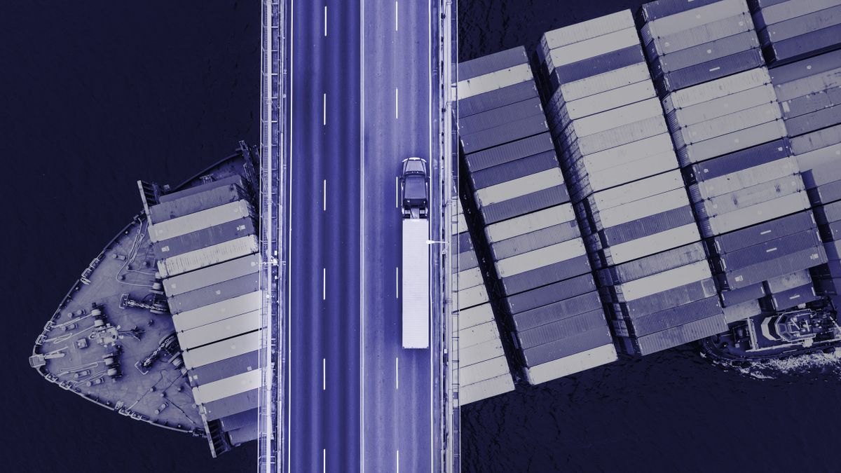 Aerial view of a container ship passing beneath a suspension bridge while a semi-truck with a cargo container crosses above.