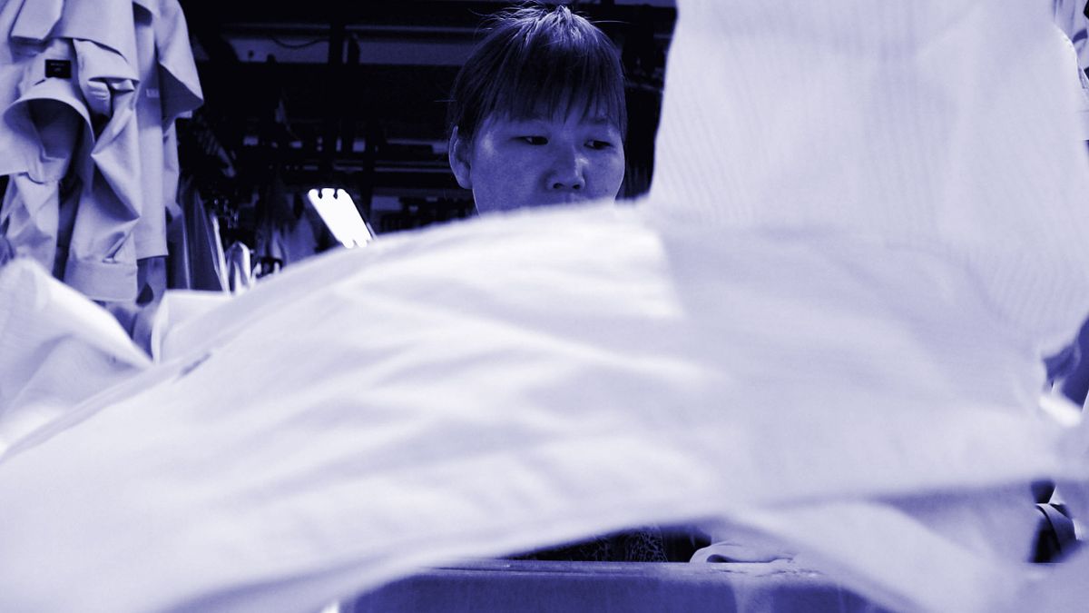 A worker is framed behind a moving shirt in a garment factory.