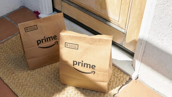 Two paper bags with the Amazon Prime logo sit on a mat outside of a door.