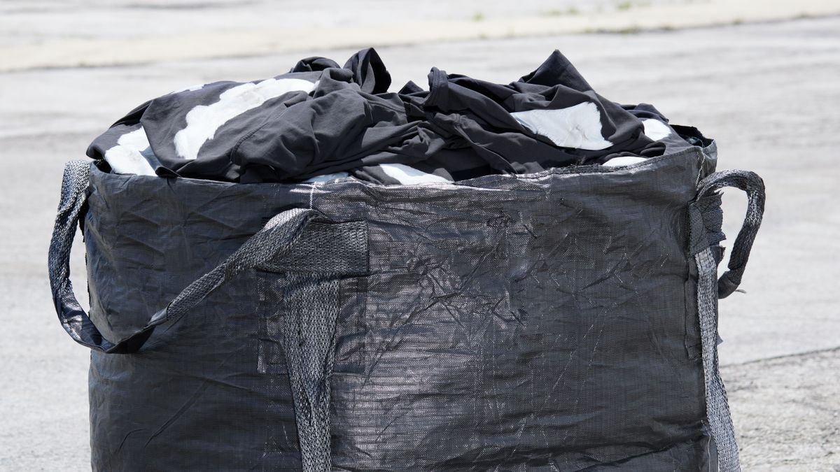 A black-and-white photo of a black plastic garbage bag with handles, filled with clothing.